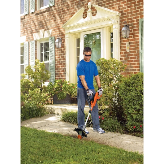BLACKDECKER LST300 string trimmer in use by a person edging a sidewalk in a residential garden.