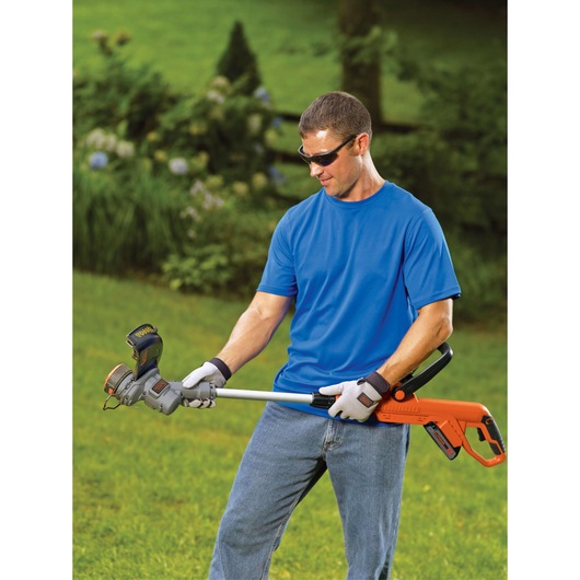 Person using BLACKDECKER LST300 string trimmer in garden, holding orange and black cordless grass trimmer.