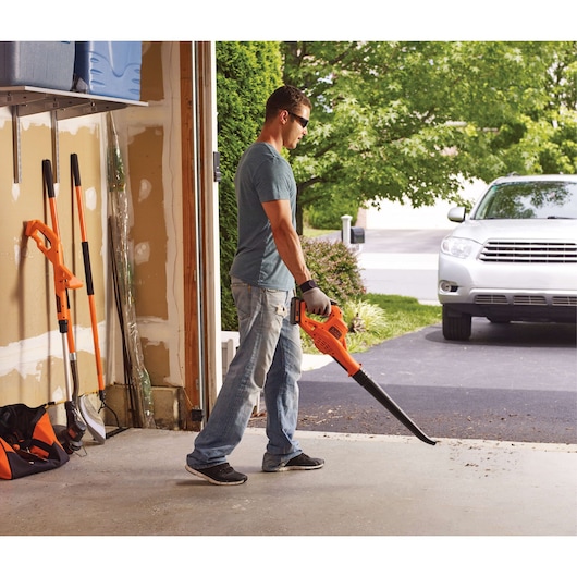 BLACKDECKER LSW221 cordless leaf blower used in a garage, orange and black colors, side view.