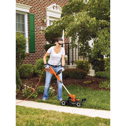 BLACKDECKER MTE912 3-in-1 trimmer and mower in use on lawn, orange and black design, photographed outdoors.