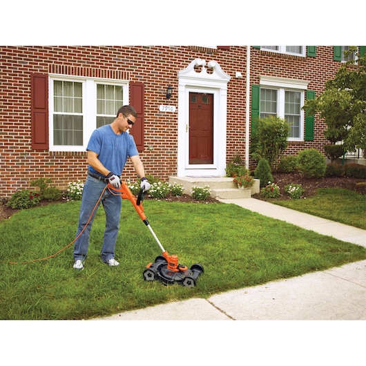 Photo of a person using a BLACK+DECKER MTE912 3-in-1 electric lawn mower and trimmer on a grassy front yard.