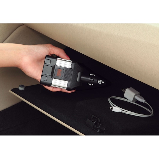BLACKDECKER PI100LA power inverter held in hand inside car glove compartment, charger and cable nearby.