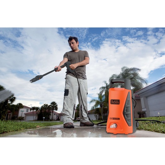 Photo of BLACKDECKER PW1370TD pressure washer in use outdoors on a driveway, orange and black compact design.