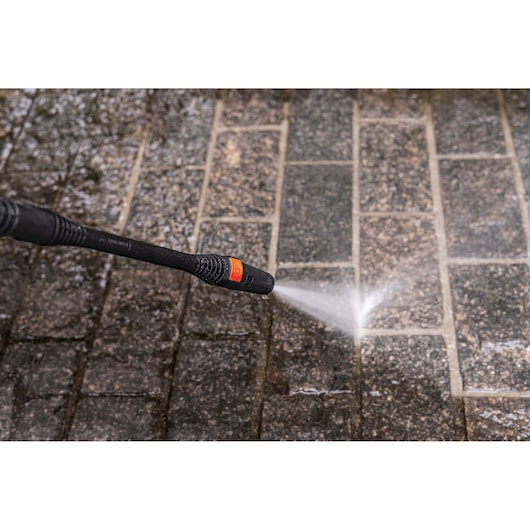 BLACKDECKER PW1450TD pressure washer nozzle spraying water onto wet stone tiles, close-up view.