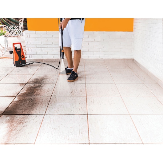 BLACKDECKER PW1450TD pressure washer cleaning tiled floor, orange unit, photo shows dirt removal.