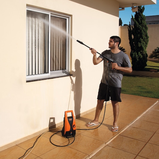 BLACKDECKER PW1450TD pressure washer cleaning window outdoors, orange and black unit on tiled patio.
