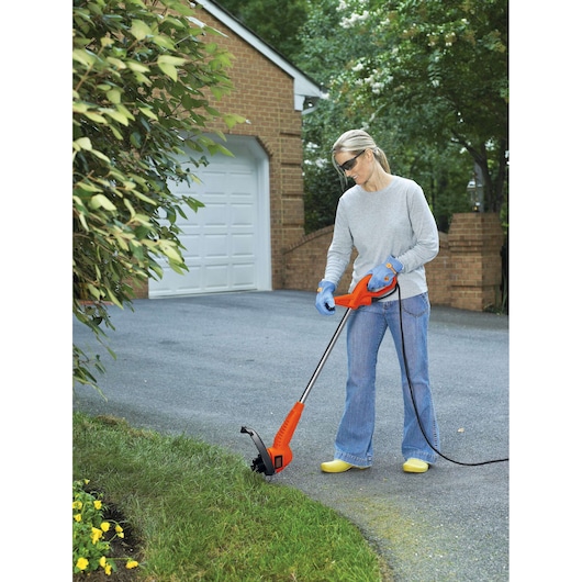 Person using BLACKDECKER ST4500 orange corded electric string trimmer on lawn edge near driveway.