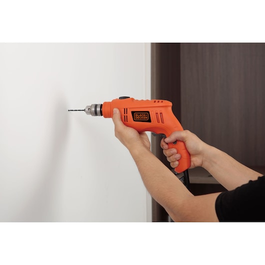 Photo of BLACKDECKER TB555 orange electric drill held by hands drilling into a white wall.
