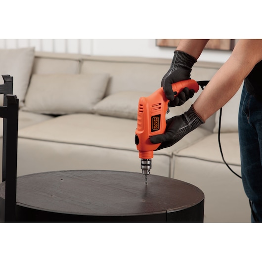 BLACKDECKER TB555 orange corded electric drill used on a round dark wood table in a living room.