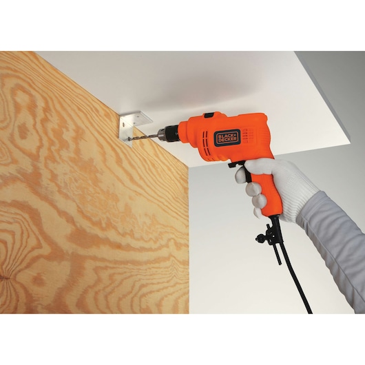 Photo of BLACKDECKER TP555 orange corded drill in use drilling metal bracket on wood panel.