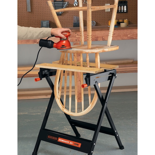 Photo of BLACKDECKER WM125 workbench holding a wooden chair being sanded in a workshop, front angle.