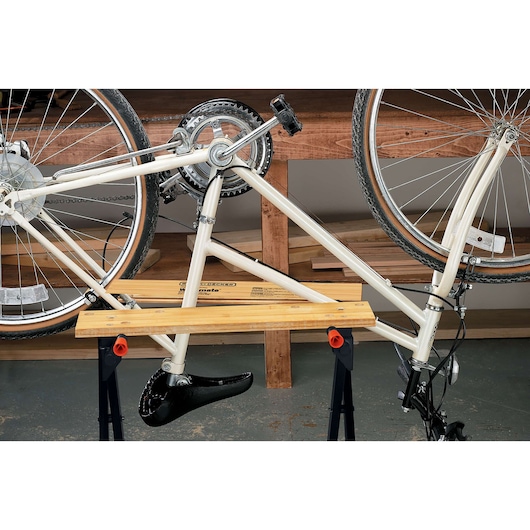 BLACKDECKER WM125 portable workbench holding a white bicycle upside down, indoor workshop setting, front angle.
